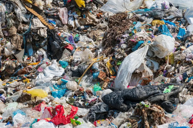 En stor bunke plastik- og tekstilaffald på lossepladsen – et symbol på udfordringerne ved lineær økonomi og behovet for cirkulær økonomi.